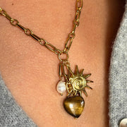 The Sunlit Charm Paperclip Necklace is the perfect blend of earthy elegance and golden glow. This 18-inch 18k gold-filled charm necklace features three standout charms: a rich brown gemstone, a radiant sun charm, and a dainty white freshwater pearl. Hypoallergenic and tarnish-free, it’s the statement piece your holiday stack has been waiting for.