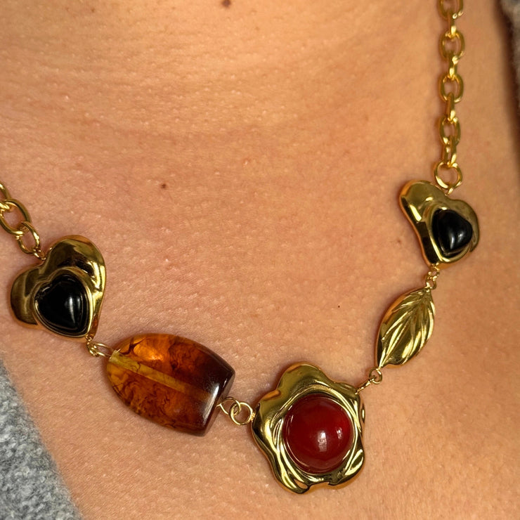 A necklace full of personality and meaning. The Boho Gem Story Necklace showcases a curated mix of charms: a brown gemstone heart, a gemstone flower centerpiece, an earthy brown stone, and a delicate gold leaf. At 18 inches, this 18k gold-filled statement necklace adds the sweetest pop of earthy tones to any outfit. Hypoallergenic, tarnish-free, and perfect for layering.