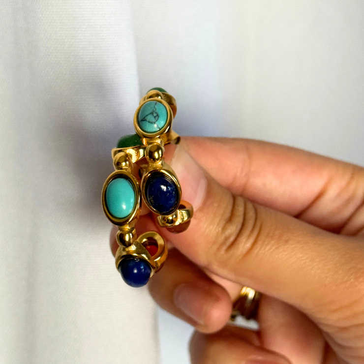 Gold ring with turquoise and blue stones held by a hand against a white background 18k gold-filled hoop with green, teal, blue, and red gemstones; hypoallergenic, tarnish-free, waterproof fall statement hoop.