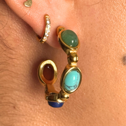 Gold hoop earrings with gemstones worn on an ear 18k gold-filled hoop with green, teal, blue, and red gemstones; hypoallergenic, tarnish-free, waterproof fall statement hoop.