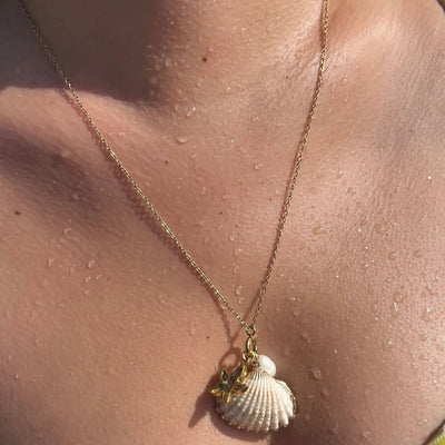 20-inch gold necklace with cockle shell, starfish, and pearl charms, styled on a breezy summer day.