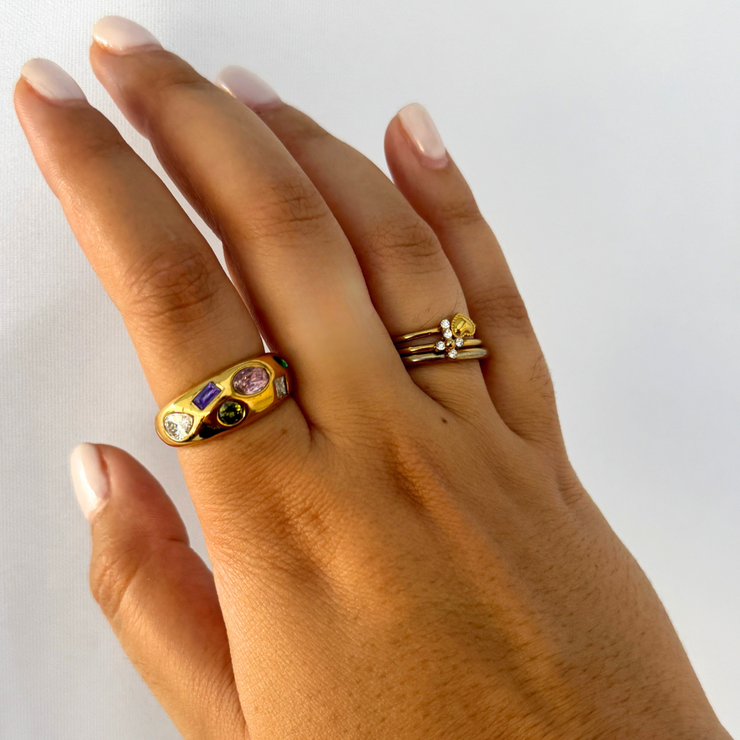 Hand wearing two gold rings with gemstones on a white background.Bold gold-filled band sprinkled with rainbow CZ stones; durable, waterproof, tarnish-free ring. 