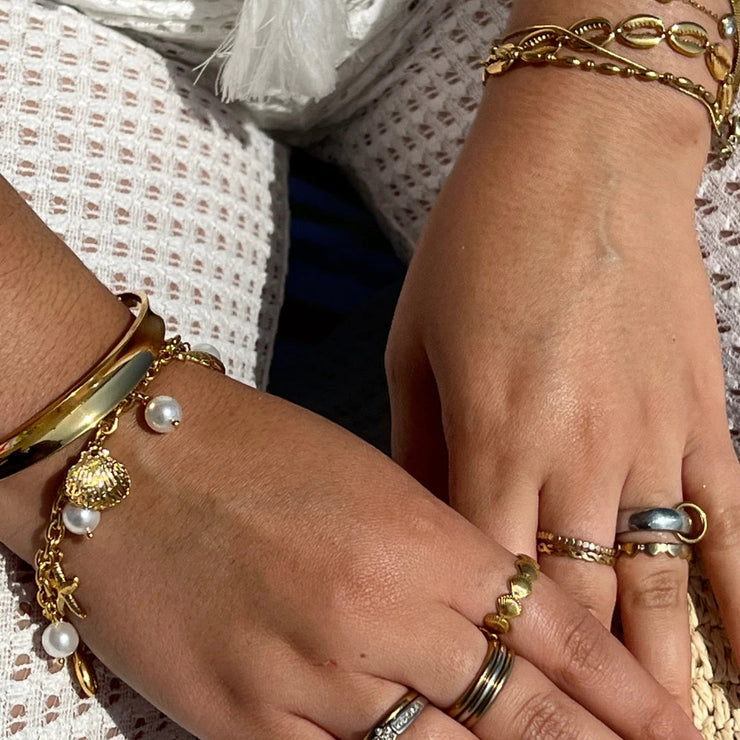 Gold charm bracelet with seashells and pearls, styled for a beach-inspired summer look.