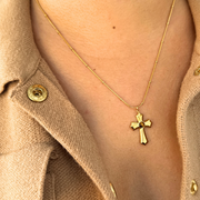 Gold necklace with a cross pendant worn by a person in a beige jacket.“Detail of lobster clasp and extender on gold-filled ball snake chain; adjustable fit for layering; Tiger’s Eye cross pendant visible.