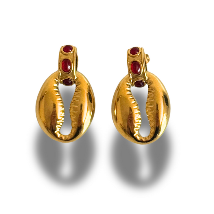Pair of gold earrings with red gemstones on a white background. Red gemstone stud with small seashell charm drop; hypoallergenic, tarnish-free coastal-meets-fall earring.