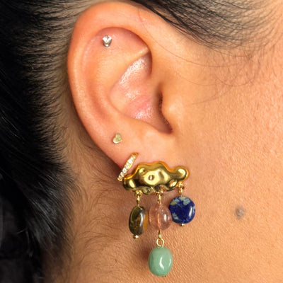 Close-up of an ear with a gold earring featuring colorful beads. cloud earrings, rainbow gemstone earrings, colorful holiday jewelry, gold cloud studs, gemstone dangle earrings, whimsical statement earrings