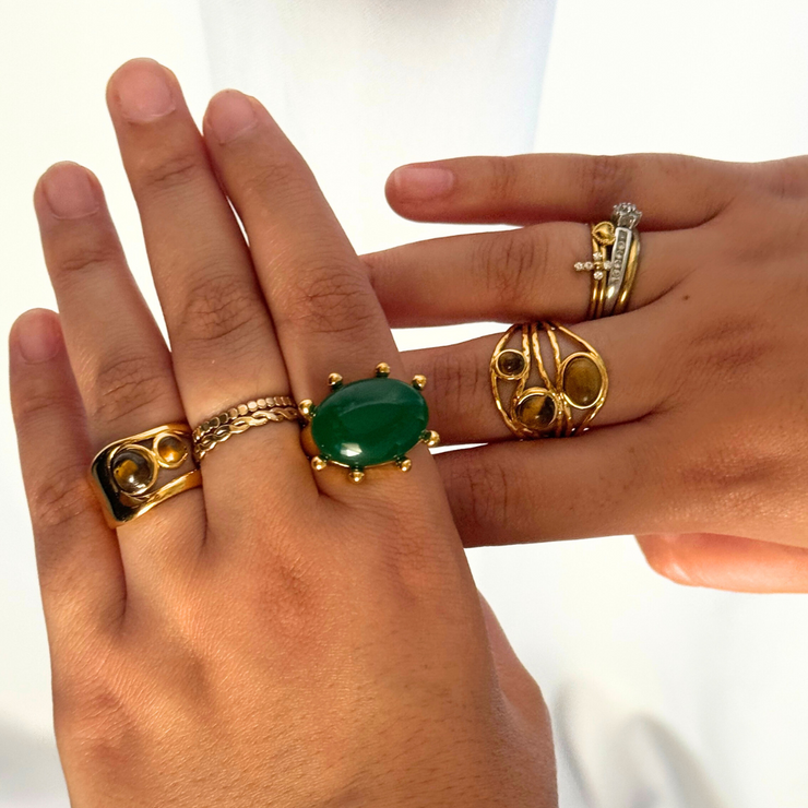 Hand wearing multiple gold rings with a green gemstone on a white background