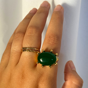 Hand wearing a green ring with gold band on a white background