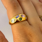 Gold ring with colorful gemstones on a person's finger against a white background. Multicolor CZ crystal statement ring in thick 18k gold-filled finish, designed for daily wear.