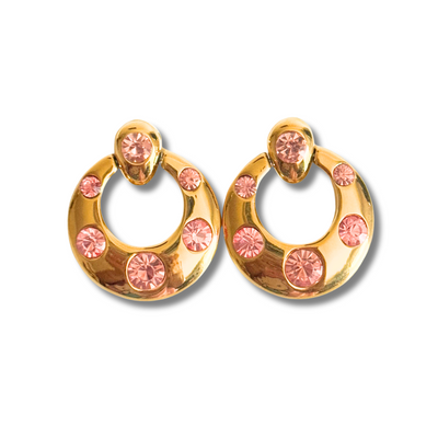 Gold hoop earrings with pink gemstones on a white background.Round vintage-inspired gold stud earring with pink CZ crystals in varying sizes, perfect for sensitive ears.18K gold-filled material, this piece is hypoallergenic, tarnish-free, and perfect for sensitive ears. The perfect accessory to elevate brunch dates, wedding guest looks, or everyday glam with a pop of pink.