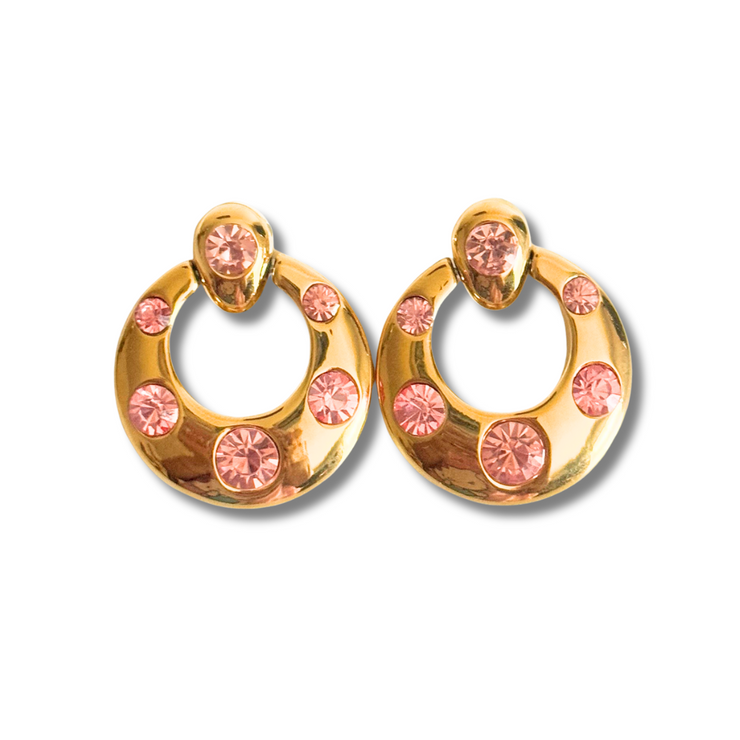 Gold hoop earrings with pink gemstones on a white background.Round vintage-inspired gold stud earring with pink CZ crystals in varying sizes, perfect for sensitive ears.18K gold-filled material, this piece is hypoallergenic, tarnish-free, and perfect for sensitive ears. The perfect accessory to elevate brunch dates, wedding guest looks, or everyday glam with a pop of pink.