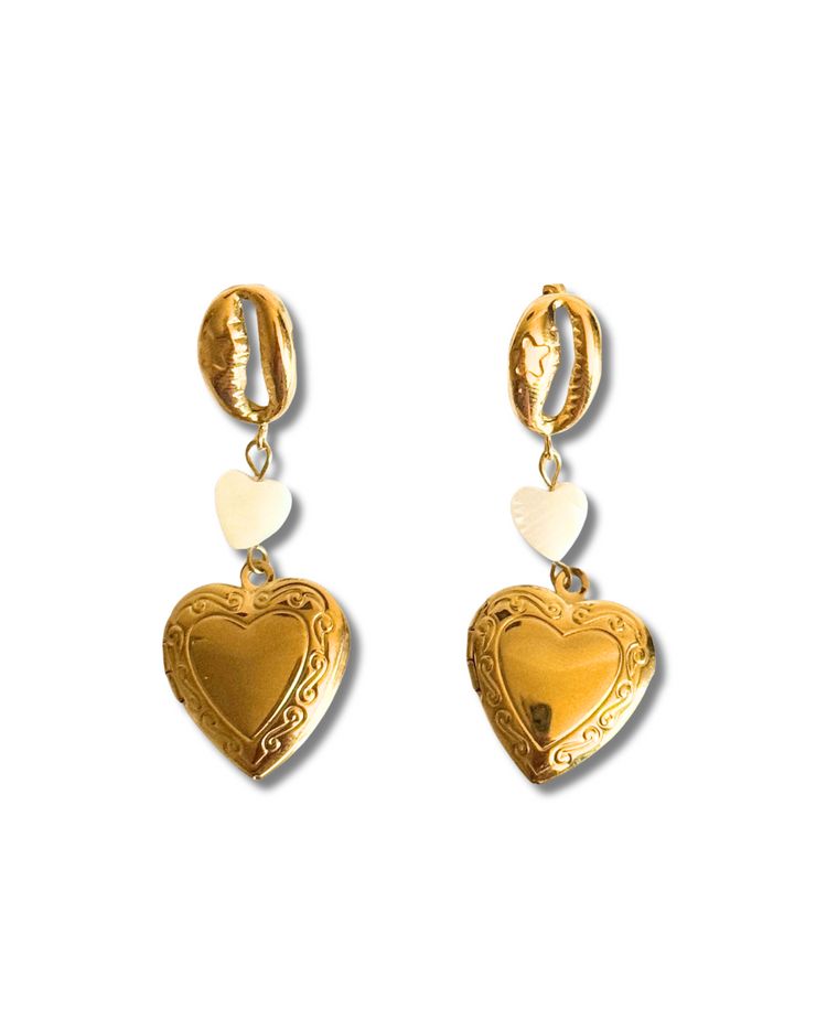 Gold heart-shaped earrings on a white background.These 18K gold-filled earrings are hypoallergenic and tarnish-free – the perfect summer statement for romantic souls and beach lovers alike.
Gold dangle earring with seashell charm, pearl heart, and heart locket, ocean-inspired