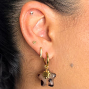 Close-up of an ear wearing a gold hoop earring with a star-shaped pendant.tortoise shell earrings, star hoops, celestial jewelry, sun and moon earrings, holiday hoops, statement tortoise earrings, boho celestial earrings