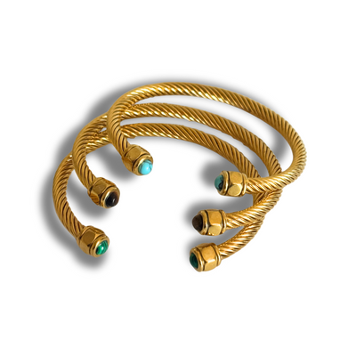 Gold bracelets with turquoise stones on a white background.Twisted 18k gold-filled open cuff on wrist with teal, brown, and green gemstone ends; adjustable, hypoallergenic design.