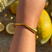 Gold wavy cuff bracelet with open space, designed to hug the wrist.