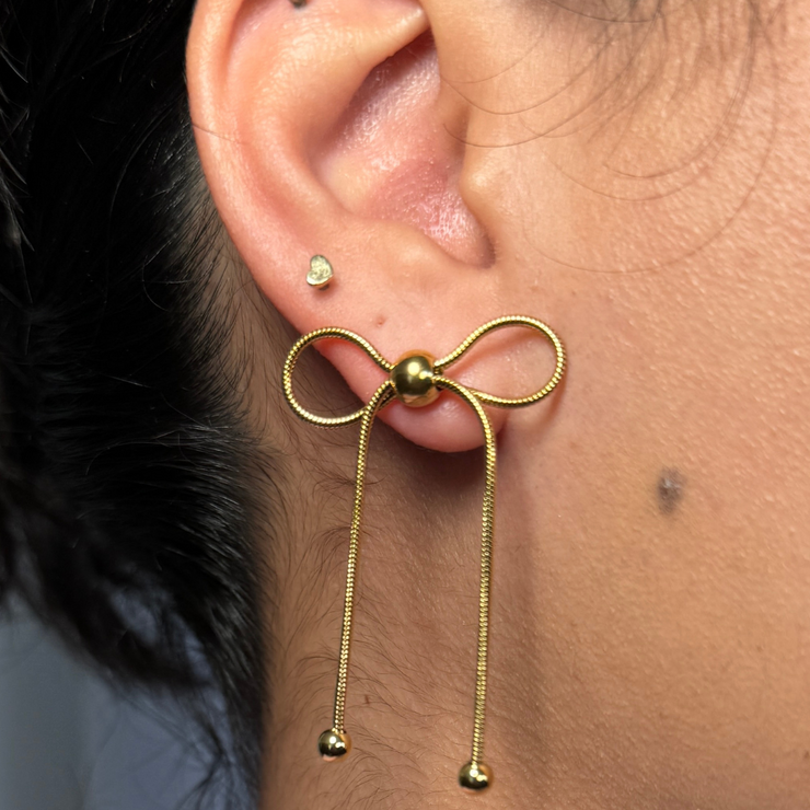 Delicate 18K gold-filled bow stud earring with dangling ends and bead accents, hypoallergenic and tarnish-free. Perfect for a romantic and elegant look.