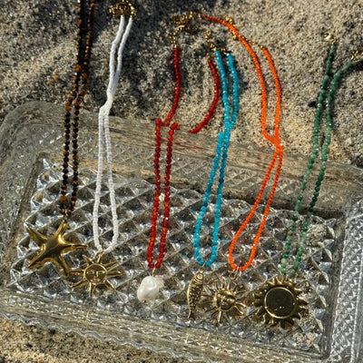 Six colorful beaded necklaces with unique charms — starfish, sun, fish, and pearl — displayed in a row