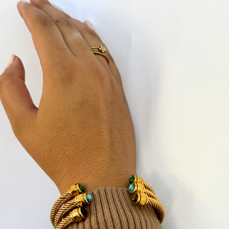 Hand wearing gold bracelets with green gemstones on a white background