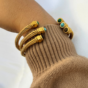 Gold bracelets with turquoise stones on a wrist against a neutral background