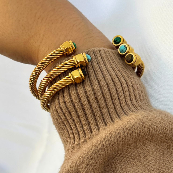 Gold bracelets with turquoise stones on a wrist against a neutral background