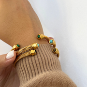 Gold bracelets with green and turquoise stones on a wrist against a white background