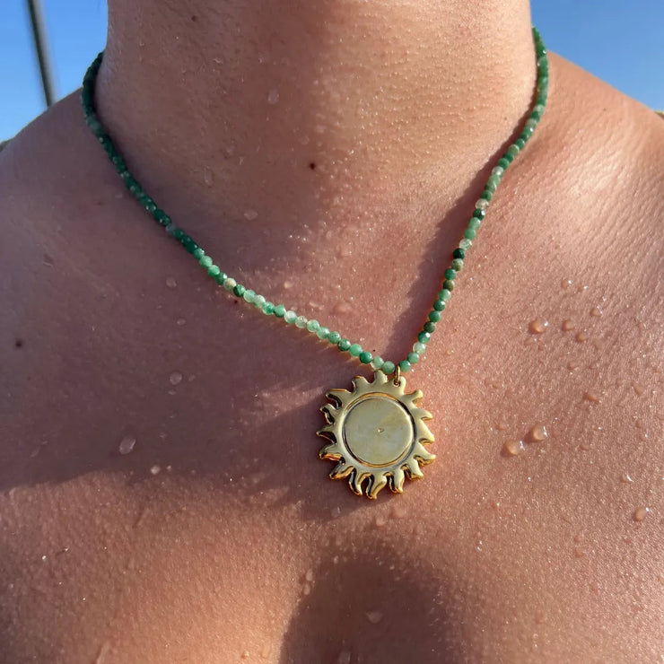 Green beaded necklace with large gold sun charm.