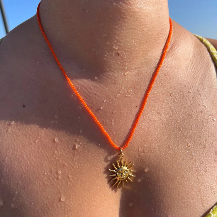 Orange beaded necklace with medium gold sun charm.